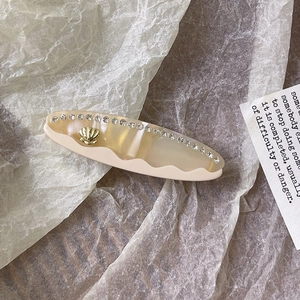 Dettaglio del fermaglio per capelli in acetato crema con conchiglia dorata e strass