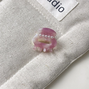Close-up of a mini purple marble hair claw clip with pearls on beige fabric