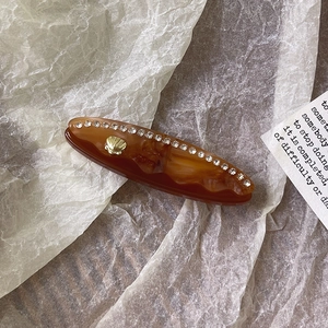 Dettaglio di un fermaglio in acetato ambrato con strass e accento a conchiglia dorata
