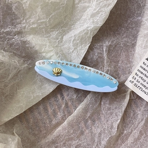 Dettaglio fermaglio in acetato a onde blu con strass e decorazione a conchiglia