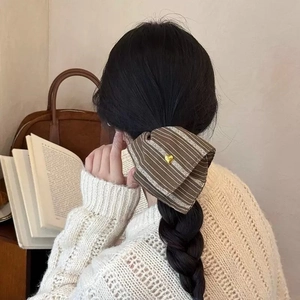 Close-up of a striped fabric scrunchie with a gold heart charm in a low braid hairstyle