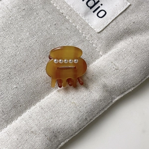 Close-up of a mini amber acetate hair claw clip featuring five white faux pearl details