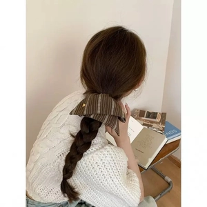 Detail view of a brown striped fabric hair tie with heart embroidery on a braided hairstyle