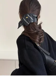 Detailed view of striped hair scrunchie with a gold heart pendant on low ponytail