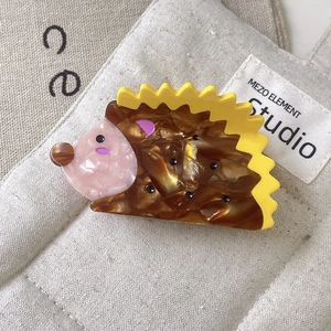 Detail of cute brown hedgehog claw clip with yellow spikes on beige canvas background