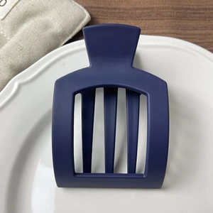 Close-up of matte dark blue hair claw with hollow square design on a white ceramic tray