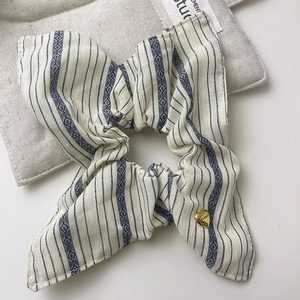 Blue and white striped scrunchie with bow and gold heart pendant on a neutral background