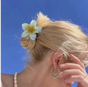 Detail van de 8cm plumeria haarklem in wit en geel gedragen op het haar tegen de blauwe lucht