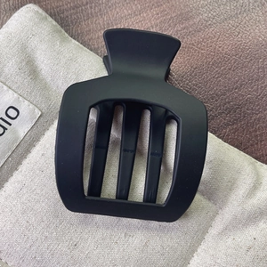Vue détaillée de la pince à cheveux carrée noire mate avec découpes sur fond en cuir