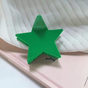 Close-up of a glossy green star-shaped hair claw clip on pink and white textured surface