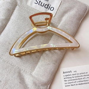 Macro detail of large gold metal hair claw clip with pearl acetate inlay on linen pouch