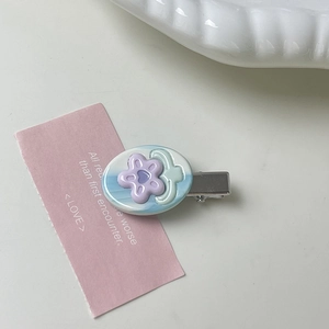 Detailed close-up of light blue oval flower hair clip on a white ceramic dish