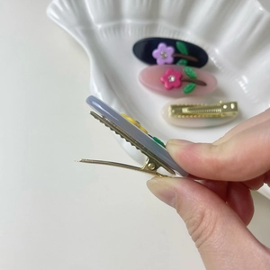 Detailed macro view showing the metal duckbill clip mechanism on a floral acetate hairpin