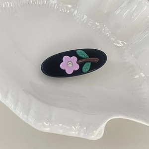 Detailed close-up of a black oval acetate hair clip with purple flower and rhinestone