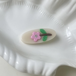 Detail of oval acetate hair clip featuring a pink rhinestone flower on a ceramic tray