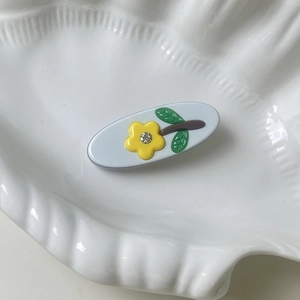 Detailed view of light blue oval acetate hair clip with yellow flower and rhinestone