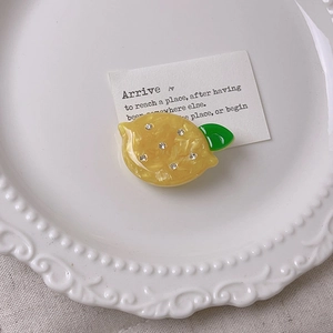 Detailed close-up of marble yellow lemon hair clip with rhinestones on a white plate