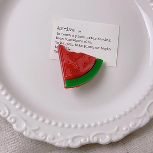 Detail view of a cute watermelon hair clip with red seeds and green rind on a ceramic tray