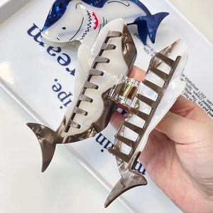 Detail of shark-shaped acetate hair claws in navy blue and brown marble finish