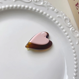 Détail d'une barrette en forme de cœur en résine rose et écaille sur un plateau blanc