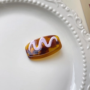 Détail d'une pince à cheveux en écaille ambrée avec décor ondulé violet sur plat