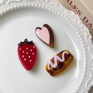 Lot de barrettes à cheveux en acétate fraise et cœur dans un plat en céramique blanc