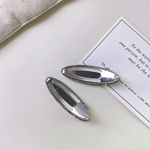 Pair of minimalist oval silver acetate hair clips in a high-polish finish on cream background