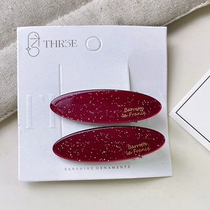 Close-up of wine red acetate hair clips with gold lettering on a display card