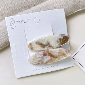 Macro detail of oval acetate hair clips with golden French lettering on marble finish