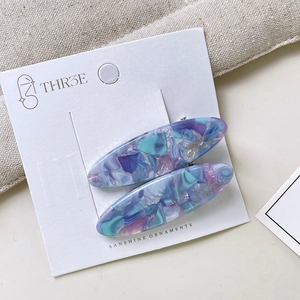 Close-up of pair of oval marble texture acetate hair clips on white brand display card