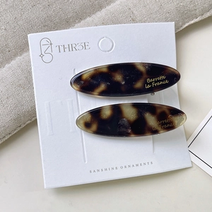 Close-up of tortoise shell oval hair clips with gold label on beige linen texture