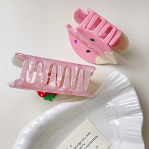 Détail de pinces à cheveux en acétate crème fraise rose sur une assiette en céramique