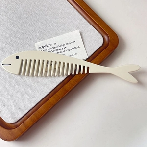 Gros plan d'un peigne à cheveux blanc crème en forme de poisson sur un plateau en bois