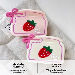 Détail d'une pince à cheveux en acétate fraise avec nœud rose sur sac en lin
