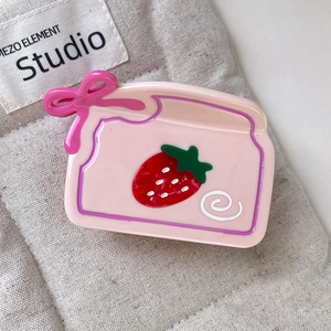 Détail de la pince à cheveux fraise rose avec nœud sur fond en lin texturé