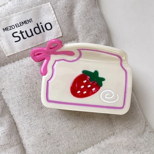 Gros plan d'une pince à cheveux motif fraise avec nœud rose sur fond en lin