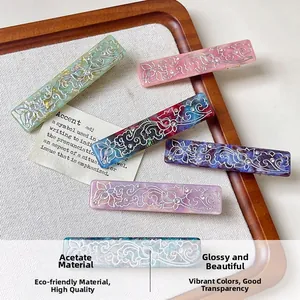 Detailed view of acetate hair clips with silver floral patterns and rhinestones in a tray