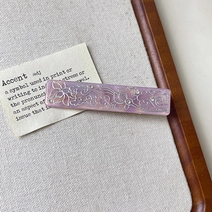 Close-up of a purple marble hair clip with silver floral patterns and small rhinestones