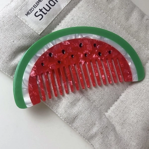 Detailed view of handmade acetate watermelon comb with glossy marbled texture on linen cloth
