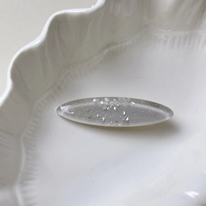 Macro shot of oval seashell texture hair clip with silver flakes on a white ceramic dish