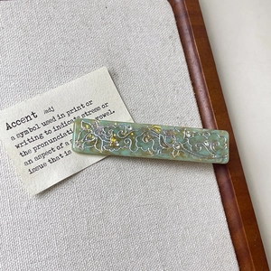 Detailed view of mint green acetate hair clip with silver lotus and cloud patterns