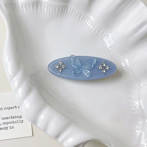 Close-up of light blue oval hair clip with resin butterfly and rhinestone accents