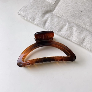 Close-up of translucent amber hair claw clip on a minimalist white desk with linen bag