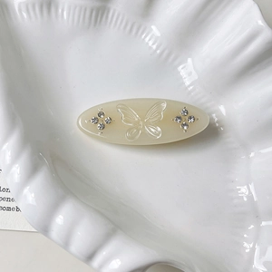 Macro detail of oval cream hair clip featuring butterfly relief and sparkling rhinestones