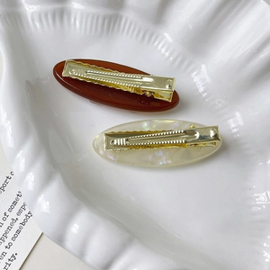 Detailed view of oval hair clips with butterfly accents and golden metal duckbill grips