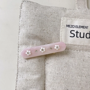 Close-up of pink resin hair clip with white floral 3D details and sparkling rhinestones