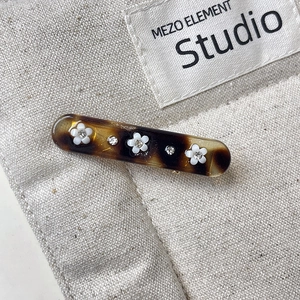 Macro shot of tortoise shell hair clip with white floral patterns and sparkling rhinestones