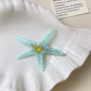 Detail of light blue starfish hair clip with gold accents on a white shell plate