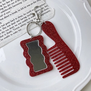 Close-up of red glitter hair comb and mirror keychain set on a decorative white tray