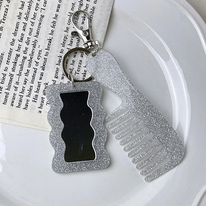 Close-up of glittery silver mini comb and mirror keychain accessory on white tray